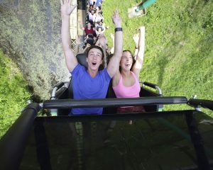 Young male and female shouting in joy with their arms up as they begin a loop on a roller coaster